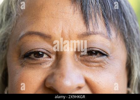 Draußen lächelt eine zweirassige Seniorin mit sanften Augen in Nahaufnahme. Ihr ausdrucksstarkes Gesicht und ihre natürliche Schönheit wurden hervorgehoben und zeigten Wärme A Stockfoto