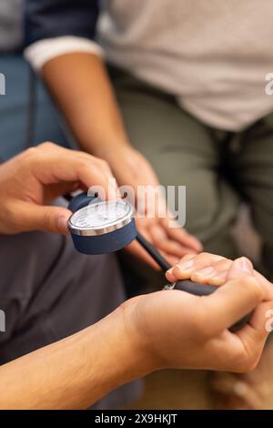 Eine männliche Krankenschwester kontrolliert zu Hause den Blutdruck einer älteren Patientin. Sie befinden sich in klinischer Umgebung, wobei medizinische Geräte im Hintergrund sichtbar sind Stockfoto