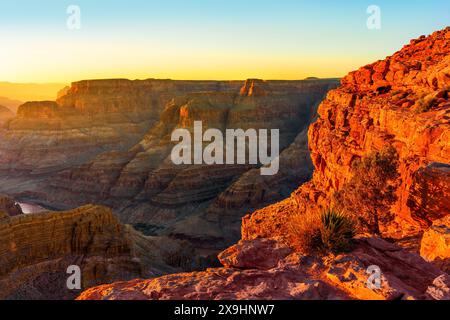 Die geschichteten Klippen und ausgedehnten Felsformationen des Grand Canyon, die bei Sonnenuntergang mit einem klaren blauen Himmel gezeigt werden. Stockfoto