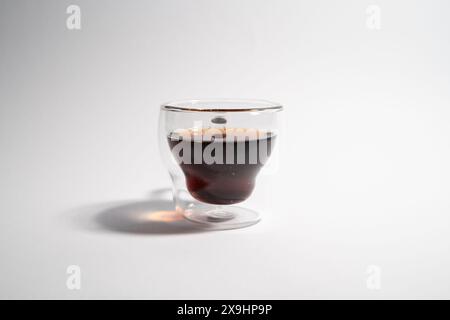 Ein Glas dunkler Flüssigkeit steht auf weißem Hintergrund. Die Flüssigkeit scheint Kaffee oder Tee zu sein, und die Tasse besteht aus Glas. Das Konzept der Ruhe und Relaxatio Stockfoto