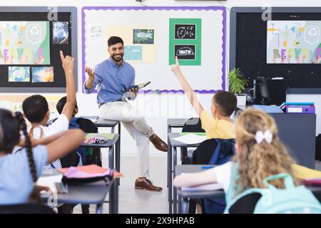 Junger asiatischer männlicher Lehrer, der eine Gruppe von Kindern in einem farbenfrohen Klassenzimmer unterrichtet Stockfoto