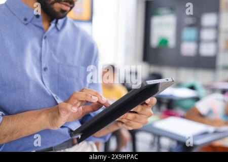 In der Schule steht ein asiatischer Lehrer mit Tablette im Fokus Stockfoto