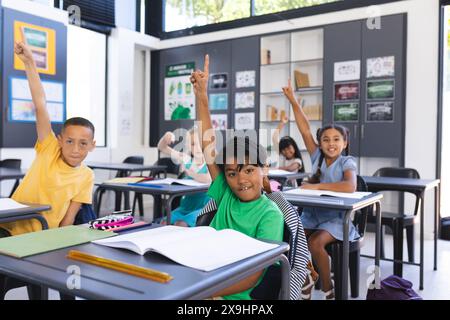 Kinder heben eifrig die Hände in einem Schulklassen Stockfoto