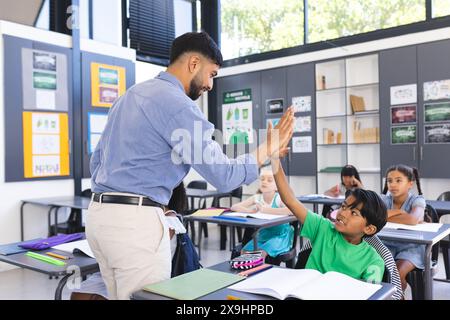 Ein junger asiatischer Lehrer, der einem Jungen mit einer Rasse in einer Schulklasse eine High-Five gibt. Lehrer und Schüler führen eine positive Interaktion mit Stockfoto