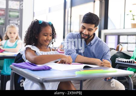 Junger asiatischer männlicher Lehrer, der ein birassisches Mädchen in einem Klassenzimmer unterrichtet Stockfoto