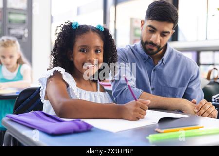 Junger asiatischer männlicher Lehrer, der ein birassisches Mädchen in einem Klassenzimmer unterrichtet Stockfoto