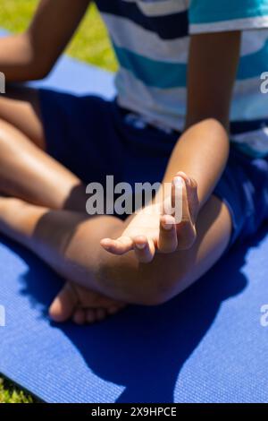 Ein birassischer Junge übt Yoga im Freien, sitzt im Kreuz auf einer blauen Matte Stockfoto