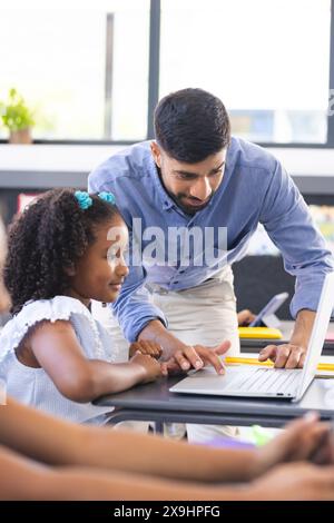 Ein junger asiatischer Lehrer hilft birassischen Mädchen bei einer Computeraufgabe Stockfoto