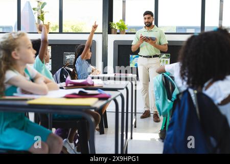 In der Schule heben junge Schüler die Hände, asiatische männliche Lehrer stehen Stockfoto