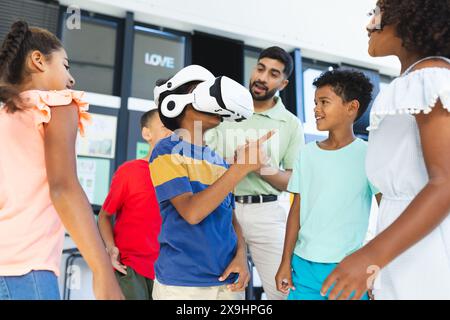 In der Schule schauen sich junge asiatische Lehrer und verschiedene Schüler eine VR-Brille an Stockfoto