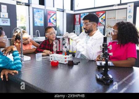 Asiatischer männlicher Lehrer zeigt drei birassische Schüler während eines Wissenschaftsexperimentes ein Reagenzglas Stockfoto