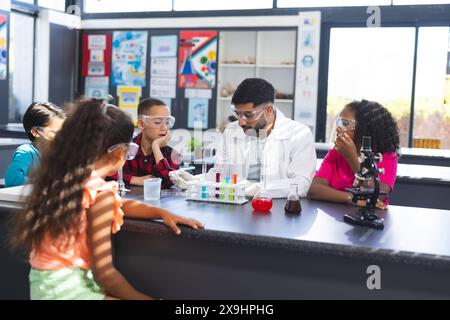 Ein junger asiatischer Lehrer führt ein wissenschaftliches Experiment mit einer Gruppe von Kindern in der Schule durch Stockfoto