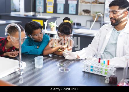 In der Schule zeigte ein asiatischer Lehrer, der junge birassische Studenten Chemiezeichen zeigte, indem er wissenschaftliche Experimente durchführte. Sie tragen eine Schutzbrille und konzentrieren sich auf Scie Stockfoto