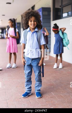 In der Schule steht ein junger afroamerikanischer Junge im Freien und lächelt mit einem Rucksack Stockfoto