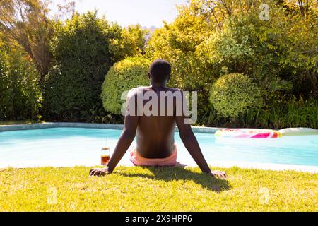 Ein junger Mann aus Afroamerikaner, der draußen sitzt und rosa Badeshorts trägt Stockfoto