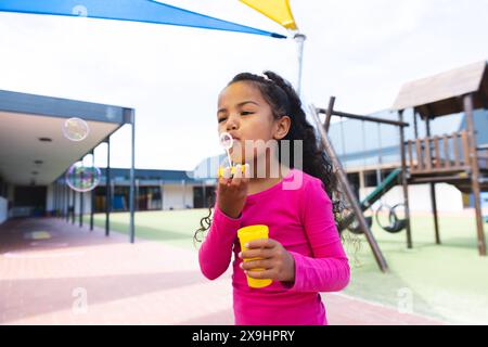 Auf dem Schulspielplatz draußen weht ein junges Mädchen, das Blasen bläst Stockfoto