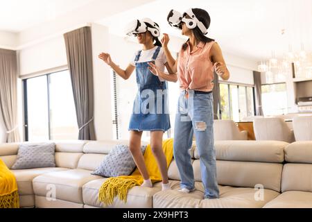 Birassische junge Schwestern, die zu Hause VR-Spiele genießen, lachen und sich bewegen Stockfoto