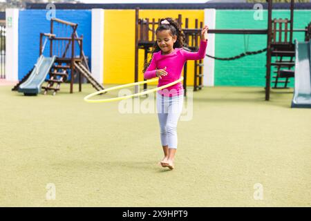 Auf dem Schulspielplatz draußen spielt ein birassisches junges Mädchen mit Hula Hoop Stockfoto