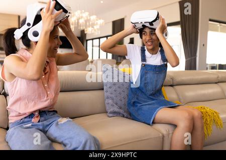 Birassische junge Schwestern, die VR-Headsets tragen und zu Hause lachen Stockfoto