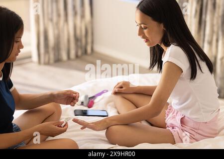 Zwei junge Schwestern zu Hause, die Nägel auf dem Bett streichen Stockfoto