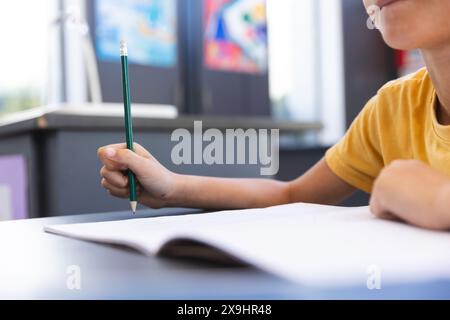 Biracial Boy konzentrierte sich auf das Schreiben in einem Klassenzimmer in der Schule Stockfoto