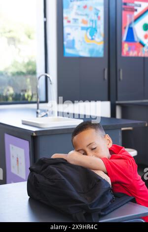 Ein birassischer Junge legt seinen Kopf in der Schule auf einen Rucksack Stockfoto