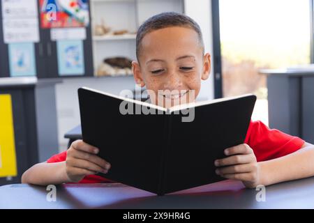 In einer Schulklasse liest ein junger birassischer Schüler ein Buch Stockfoto