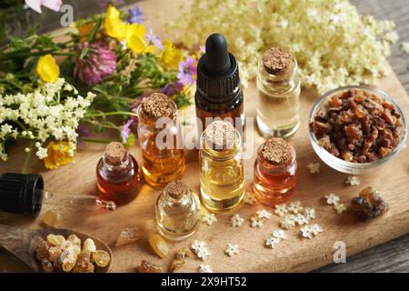 Ätherische Öle, Myrrhe, Weihrauch und verschiedene Frühlingsblumen auf einem Holztisch Stockfoto