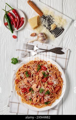 Garnelen fra diavolo mit Spaghetti, Tomatensoße, bestreut mit geriebenem Parmesankäse auf weißer Platte auf weißem Holztisch, vertikale Ansicht fr Stockfoto