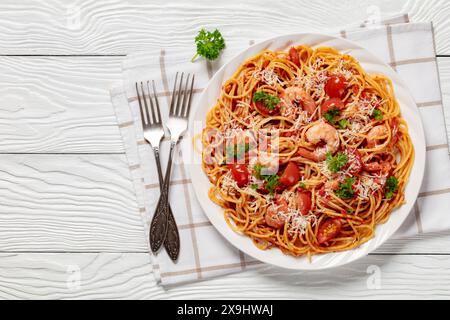 Garnelen fra diavolo mit Spaghetti, Tomatensoße, bestreut mit geriebenem Parmesankäse auf weißer Platte auf weißem Holztisch mit Gabeln, horiz Stockfoto