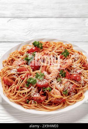 Garnelen fra diavolo mit Spaghetti, Tomatensoße, bestreut mit geriebenem Parmesankäse auf weißer Platte auf weißem Holztisch, vertikale Ansicht fr Stockfoto