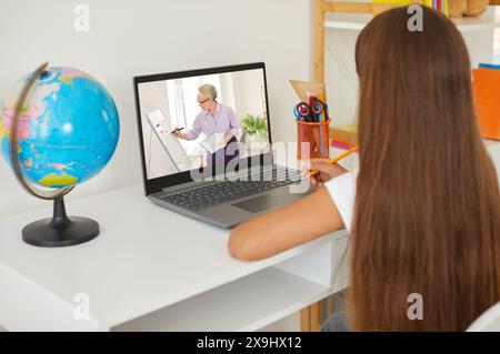 Schulmädchen sieht Online-Unterricht auf Laptop, sitzt am Schreibtisch, Online-Unterricht zu Hause. Stockfoto