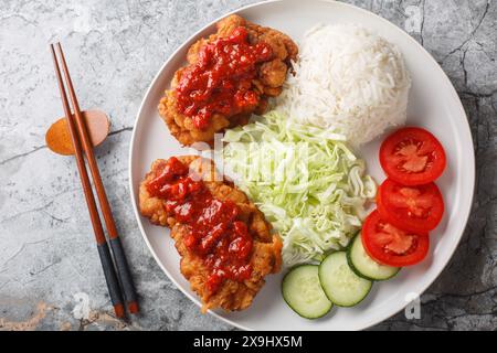 Ayam geprek ist ein typisch indonesisches Gericht mit gebratenem Huhn mit Sambal, serviert mit weißem Reis, Gurke, Tomaten und Kohl in der Nähe auf dem Teller Stockfoto