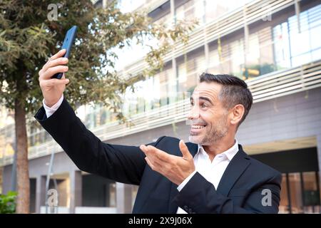 Porträt eines lächelnden Geschäftsmannes, der draußen ein Foto mit einem Smartphone macht. Stockfoto