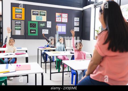 In der Schule heben die Schüler an den Schreibtischen die Hände, der Lehrer steht ihnen gegenüber im Klassenzimmer Stockfoto
