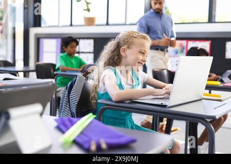 In der Schule gibt es verschiedene Gruppen junger Schüler, die sich im Klassenzimmer auf Laptops konzentrieren Stockfoto