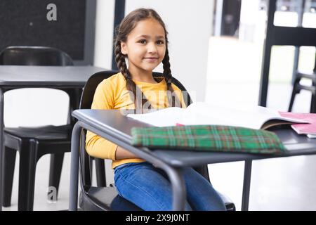 In der Schule sitzt eine junge, birassische Schülerin in einem Klassenzimmer und liest ein Buch Stockfoto