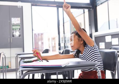 Birassisches Mädchen mit heller Haut, dunklem Haar hebt die Hand in der Klasse, Kopierraum Stockfoto