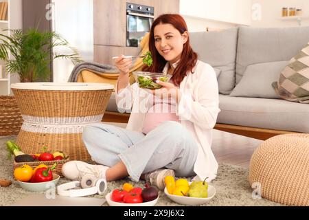 Junge schwangere Frau, die zu Hause frischen Gemüsesalat isst Stockfoto