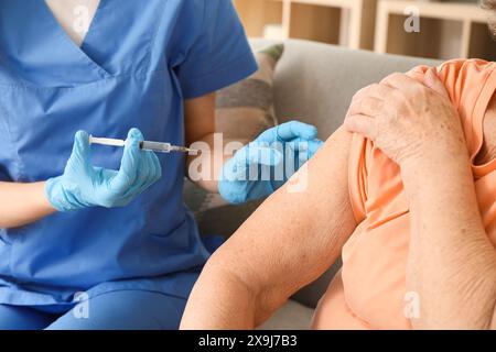 Junge Krankenschwester geimpft ältere Frau auf Sofa zu Hause, Nahaufnahme Stockfoto