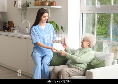Junge Krankenschwester, die der Seniorin in der Küche Pillen und ein Glas Wasser gibt Stockfoto