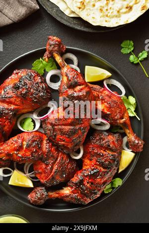 Tandoori-Hühnchen im indischen Stil auf dem Teller mit dunklem Steinhintergrund. Hähnchenschenkel mariniert in Joghurt und Gewürzen. Draufsicht, flach liegend Stockfoto