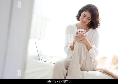 Frau, die auf dem Bett saß, mit Laptop-Computer und lächelte. Stockfoto