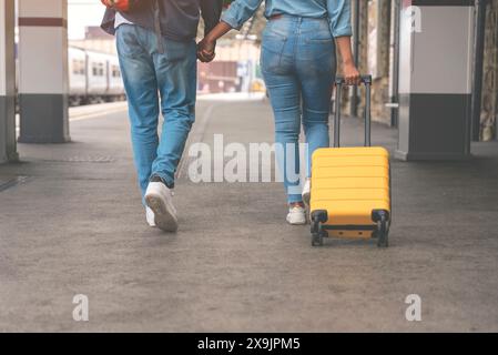 Glückliches, liebevolles Paar mit Gepäck und Rucksack, das auf dem Bahnsteig entlang läuft, während sie bereit sind, in den Urlaub zu reisen. Mann und Frau, die Hände halten Stockfoto