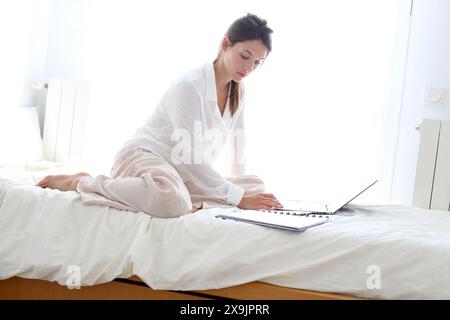 Frau, die auf dem Bett sitzt und einen Laptop benutzt. Stockfoto