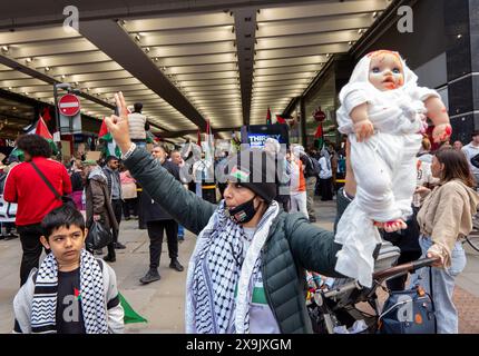 Eine Frau hält eine Puppe auf der Marktstraße. Palästinensische Demonstration im Stadtzentrum von Manchester. Der Protest sah Demonstranten die Marktstraße entlang an einer Filiale der Barclays Bank vorbeiziehen, die nach dem Zerschlagen von Fenstern an Bord ging und das Gebäude mit roter Farbe bedeckt war, als Teil eines Protestes gegen die Beteiligung der Banken an Investitionen in Israel. Manchester, UK Bild: Garyroberts/worldwidefeatures.com Stockfoto