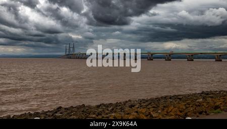 Blick auf die zweite Severn Crossing, offiziell die Prince of Wales Bridge genannt, unter einem bewölkten Himmel mit trübem Wasser und felsiger Küste Stockfoto