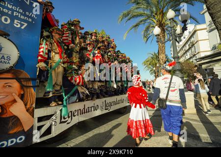 Karneval in Cádiz, Spanien (Carnaval de Cádiz). Festivalkünstler in Karnevalskostümen feiern auf dem Paradewagen, während Partygäste an der Band vorbeischlendern. Stockfoto