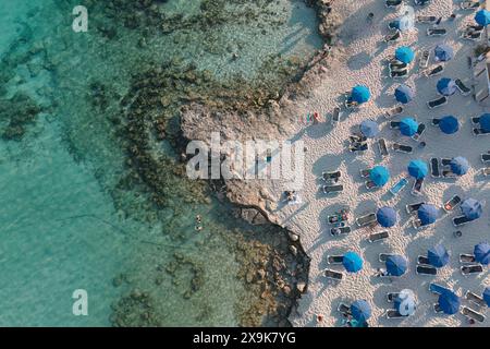 Top-down-Aufnahme eines Nissi-Strandes mit klarem türkisfarbenem Wasser, Sonnenliegen und blauen Sonnenschirmen. Ayia Napa, Zypern Stockfoto