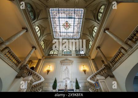 Im Rathaus von Valencia (Ayuntamiento de València). Innenraum einer großen Treppe mit Buntglasdecke mit Stadtwappen, Fledermaus und Kronwappen. Stockfoto